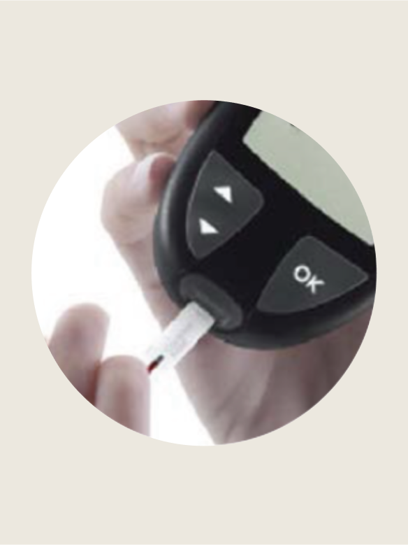 Hand holds a glucose meter inserting a test strip, with buttons labeled "OK" in a bright environment.